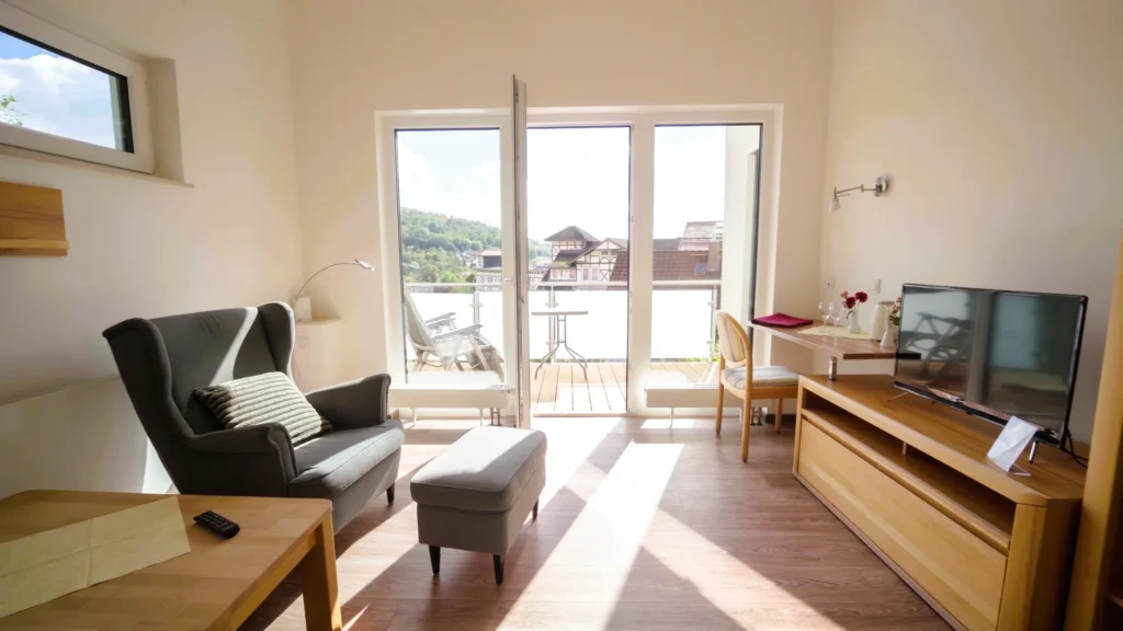 Das Wohnzimmer von Appartement 2 bietet Sofa, Sessel, Fernseher und eine geöffnete Tür zum sonnigen Balkon. Das Wohnzimmer von Appartement 2 bietet Sofa, Sessel, Fernseher und eine geöffnete Tür zum sonnigen Balkon.
