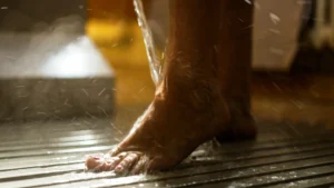 Ein Wasserstrahl läuft bei einem Kneipp-Beinguss über Unterschenkel und Fuß auf einen gerillten Boden. Ein Wasserstrahl läuft bei einem Kneipp-Beinguss über Unterschenkel und Fuß auf einen gerillten Boden.