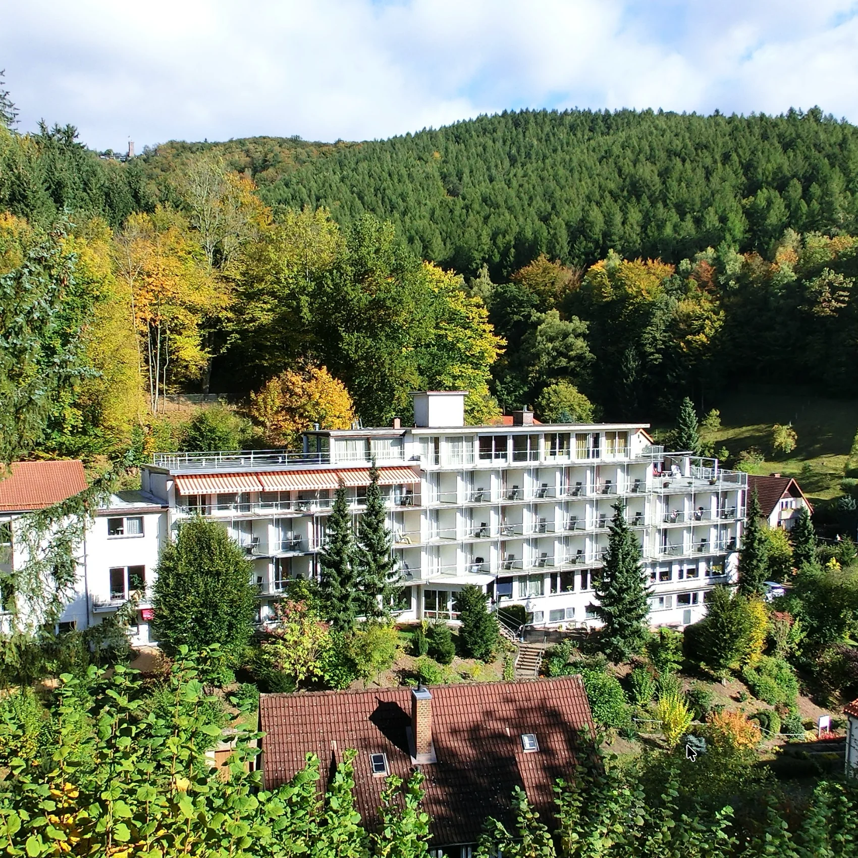 Das Vitalium mit seiner weißen Balkonfassade steht zwischen grünen Bäumen unterhalb eines bewaldeten Bergrückens in Bad Lauterberg. Das Vitalium mit seiner weißen Balkonfassade steht zwischen grünen Bäumen unterhalb eines bewaldeten Bergrückens in Bad Lauterberg.