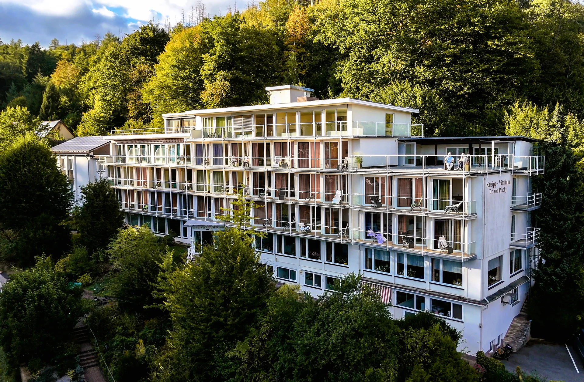 Abendlicht fällt auf die weiße Balkonfassade des Vitaliums vor den dicht bewachsenen Hängen in Bad Lauterberg